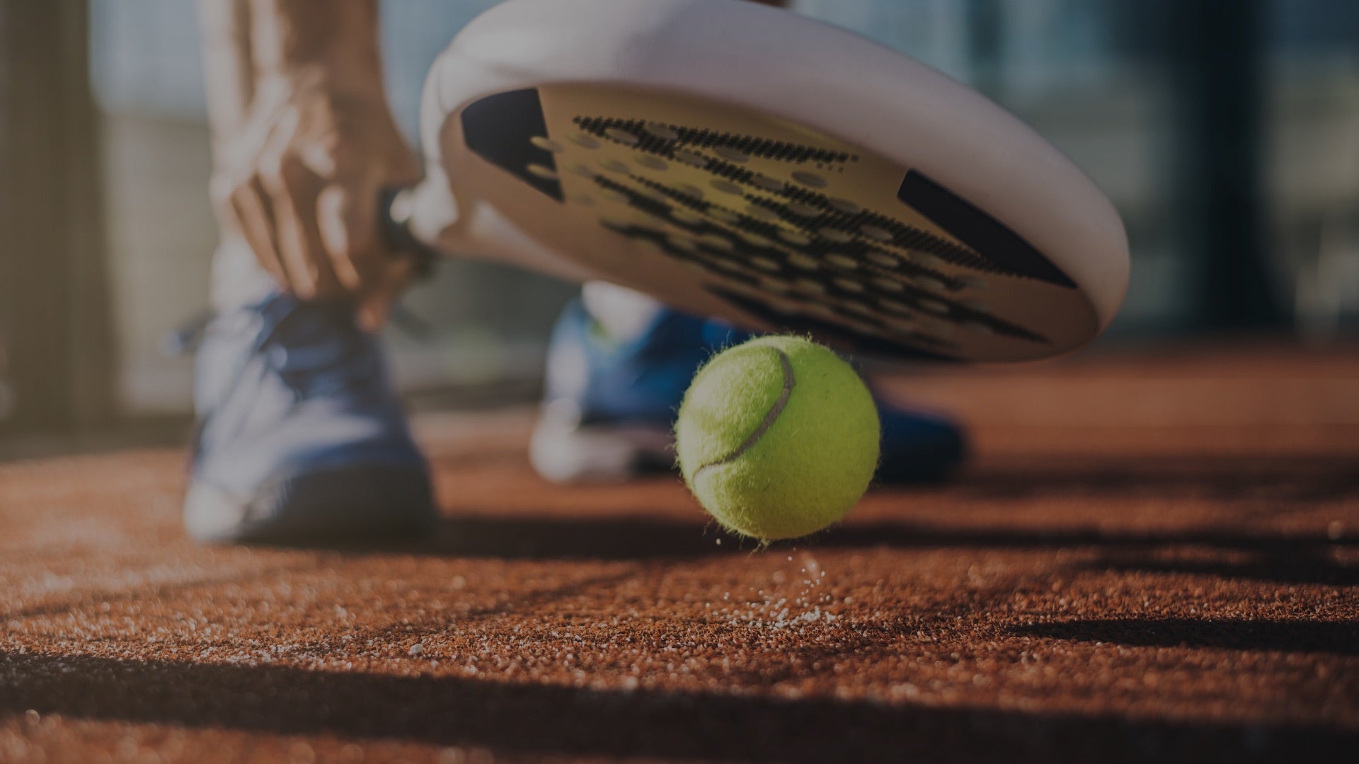 Padel racquet and ball on a clay court with a player's foot in the background - MatchSet Racquet Sports